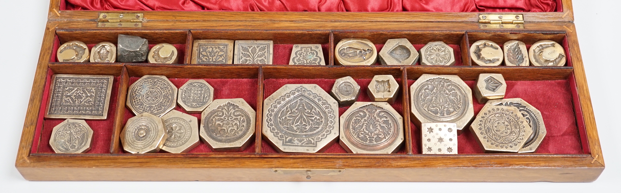 A cased group of Indian or Afghan brass seals or stamps, case 45.5cm wide, 14cm deep